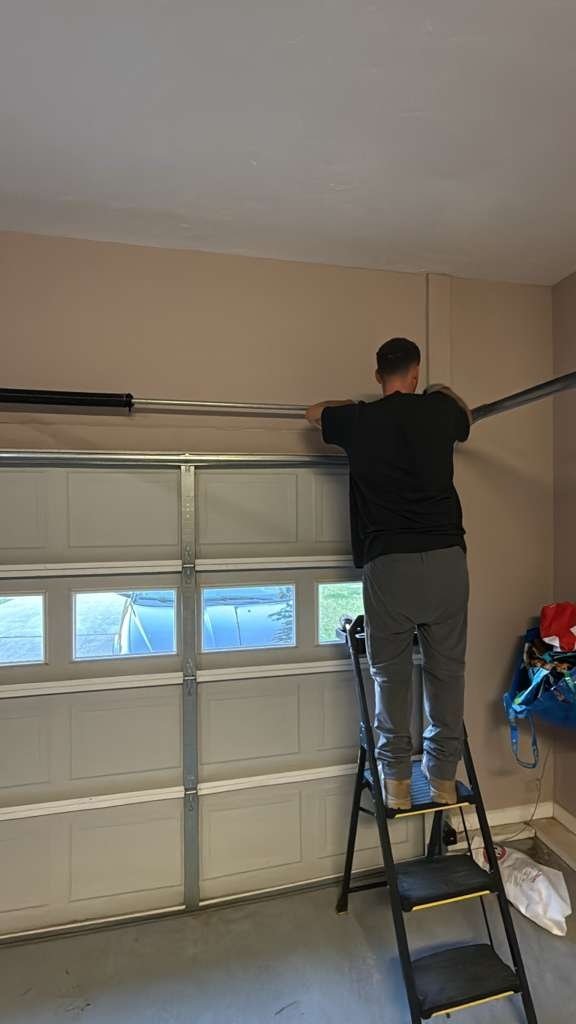 Worker on a stepladder reaching across the spring bar above a door