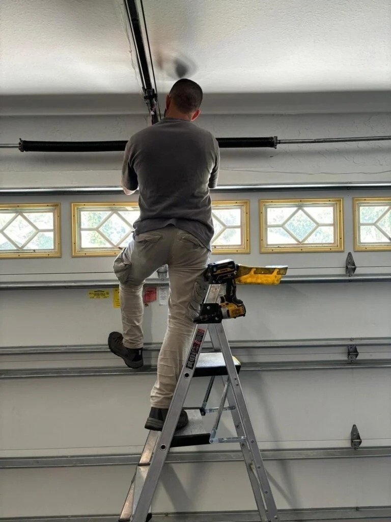 Worker on a ladder in front of a white door with a row of windows