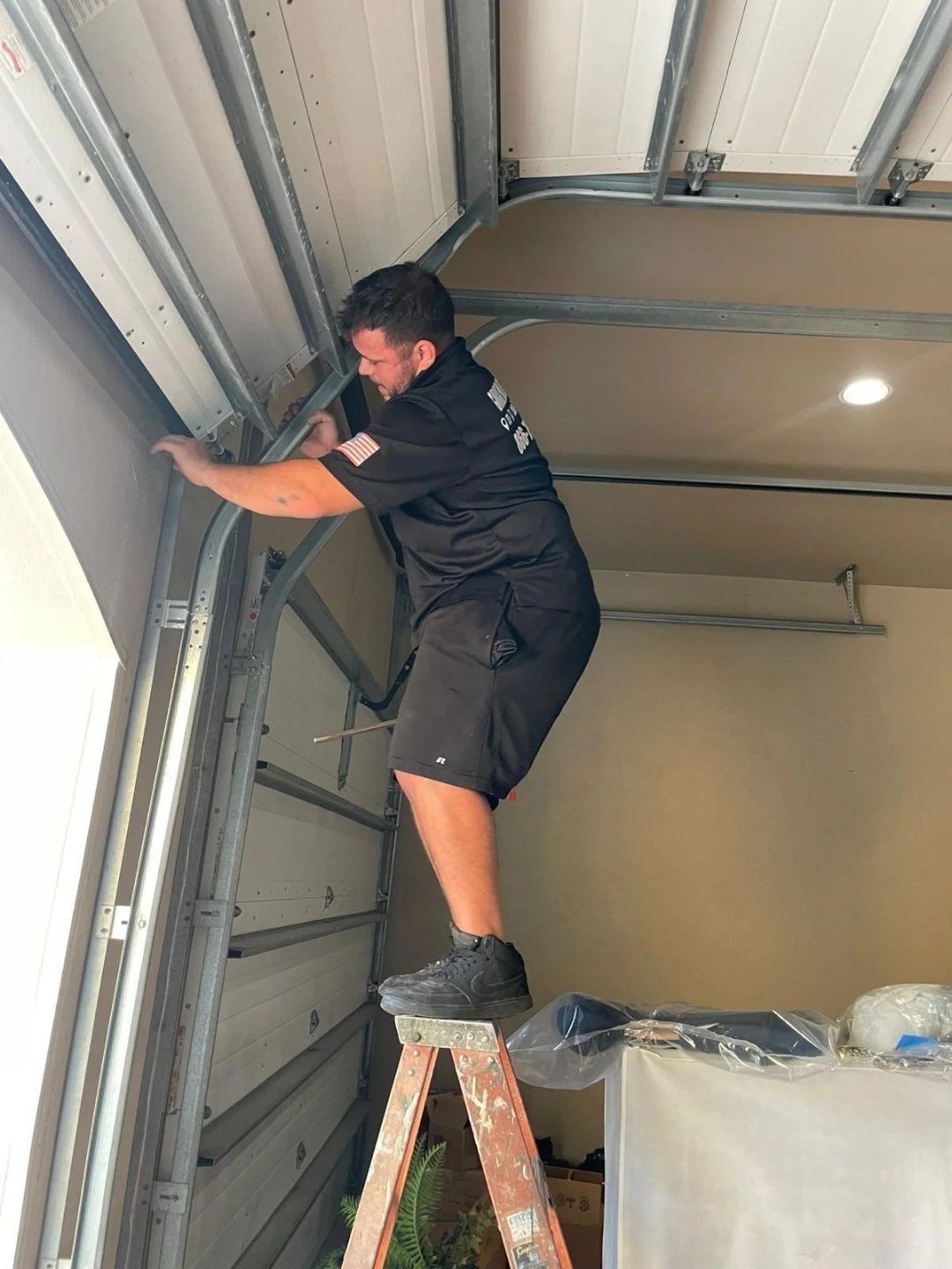 Worker on a ladder at the upper corner of a garage opening