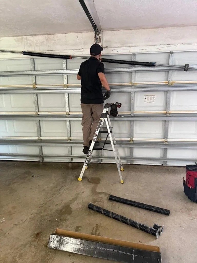 Worker on a ladder beneath a spring bar, with removed springs on the floor