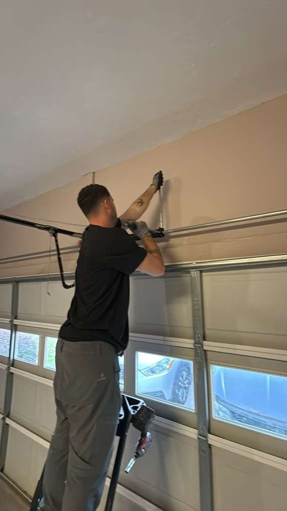 Worker on a ladder tightening a ceiling bracket above a garage door