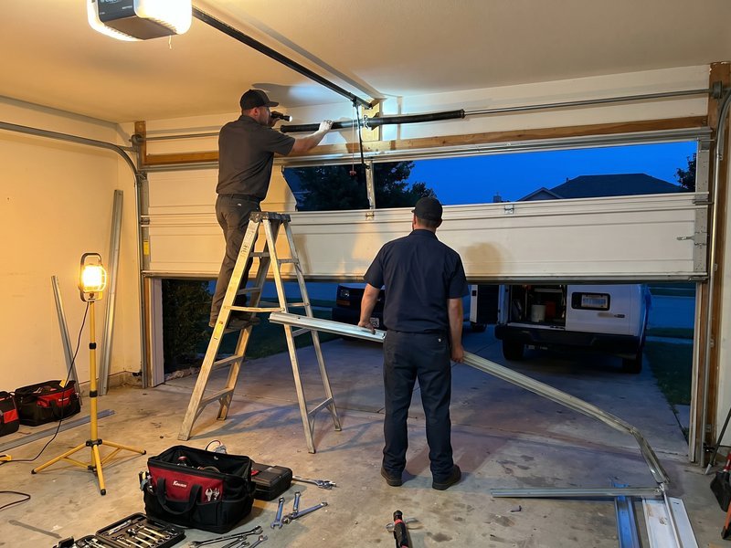 Workers with a ladder beneath a partly raised garage door in evening light