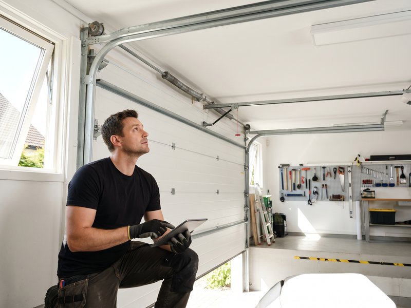 Worker holding a tablet in front of a white sectional door