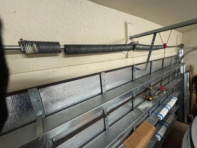Close view of a torsion spring, shaft and lift cables above a sectional door